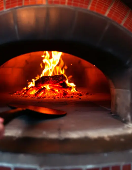 The mouth of the wood-fired brick oven, flames and embers glowing