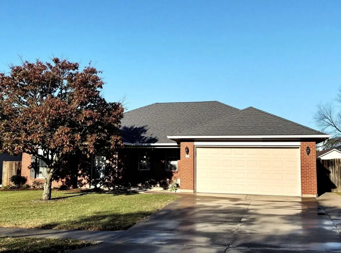 After: the same house with a new charcoal architectural shingle roof and clean gutters, under a blue sky