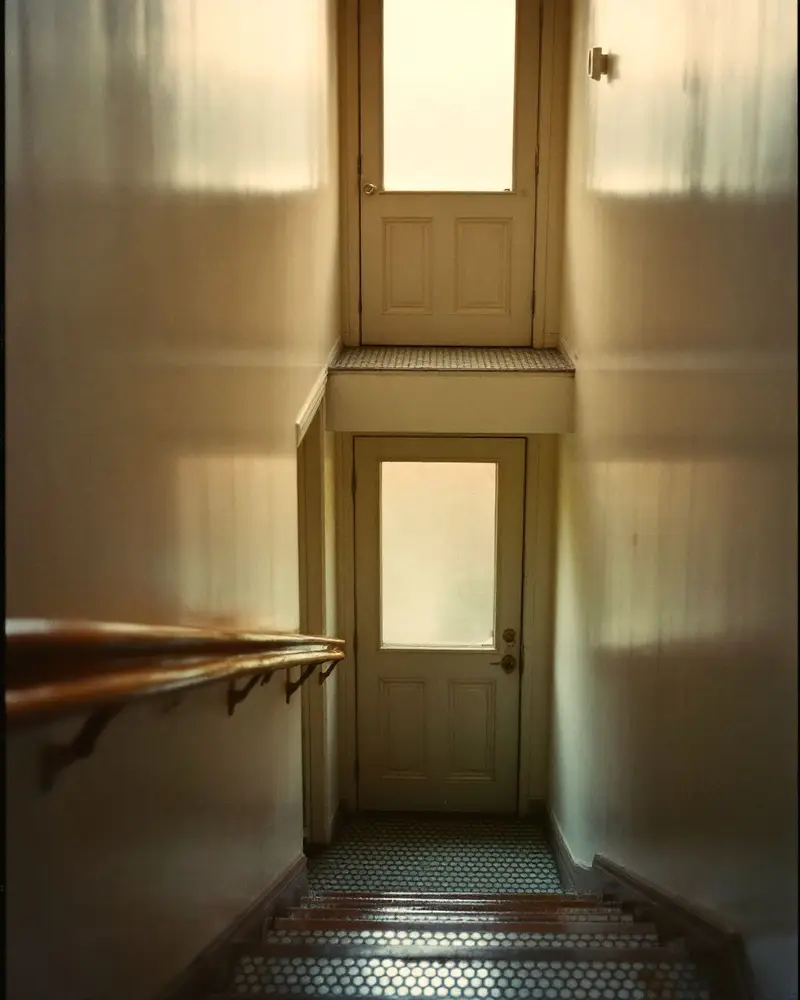 A narrow old stairway with a wooden handrail leading up to a frosted glass office door